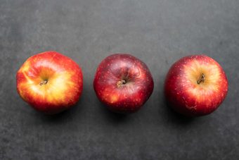 Drei rote Äpfel nebeneinander auf dunkelgrauem Untergrund