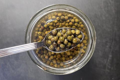 Eingelegter grüner Pfeffer im Glas mit einem Löffel voll Körner