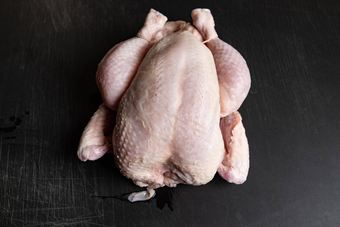 Ganzes rohes Hähnchen auf einem dunklen Schneidebrett
