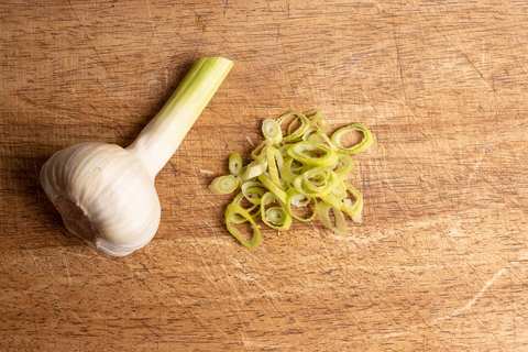 Junger Knoblauch mit grünem Trieb, daneben in feine Ringe geschnitten