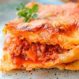 Lasagne angeschnitten auf dem Teller, zwischen den Platten sichtbar viel Hackfleischsauce