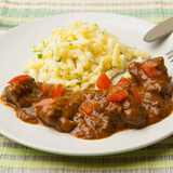 Rindergulasch serviert mit Spätzle, Petersilie und Tomatenwürfel