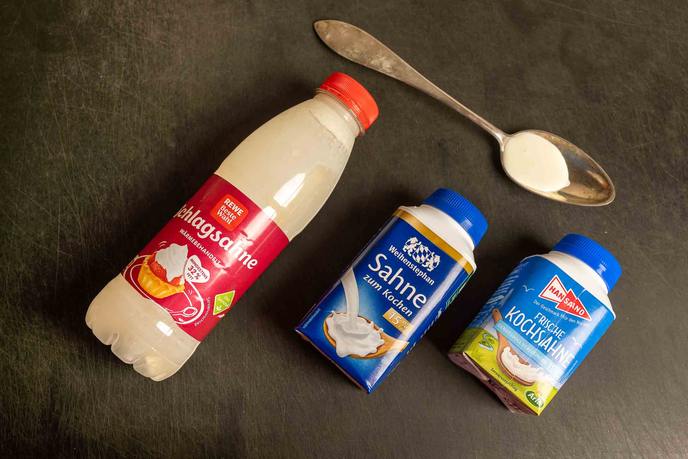 Drei Sahnepackungen und ein Löffel mit Sahne von oben fotografiert