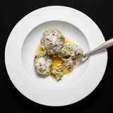 Spinatknödel mit zerlassener Butter und frisch geriebenem Käse auf weißem Teller angerichtet