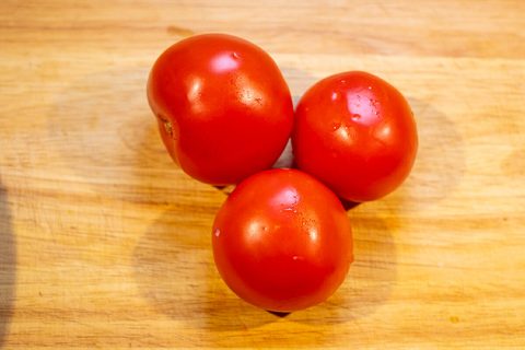 Drei runde rote Tomaten auf einem Holzbrett